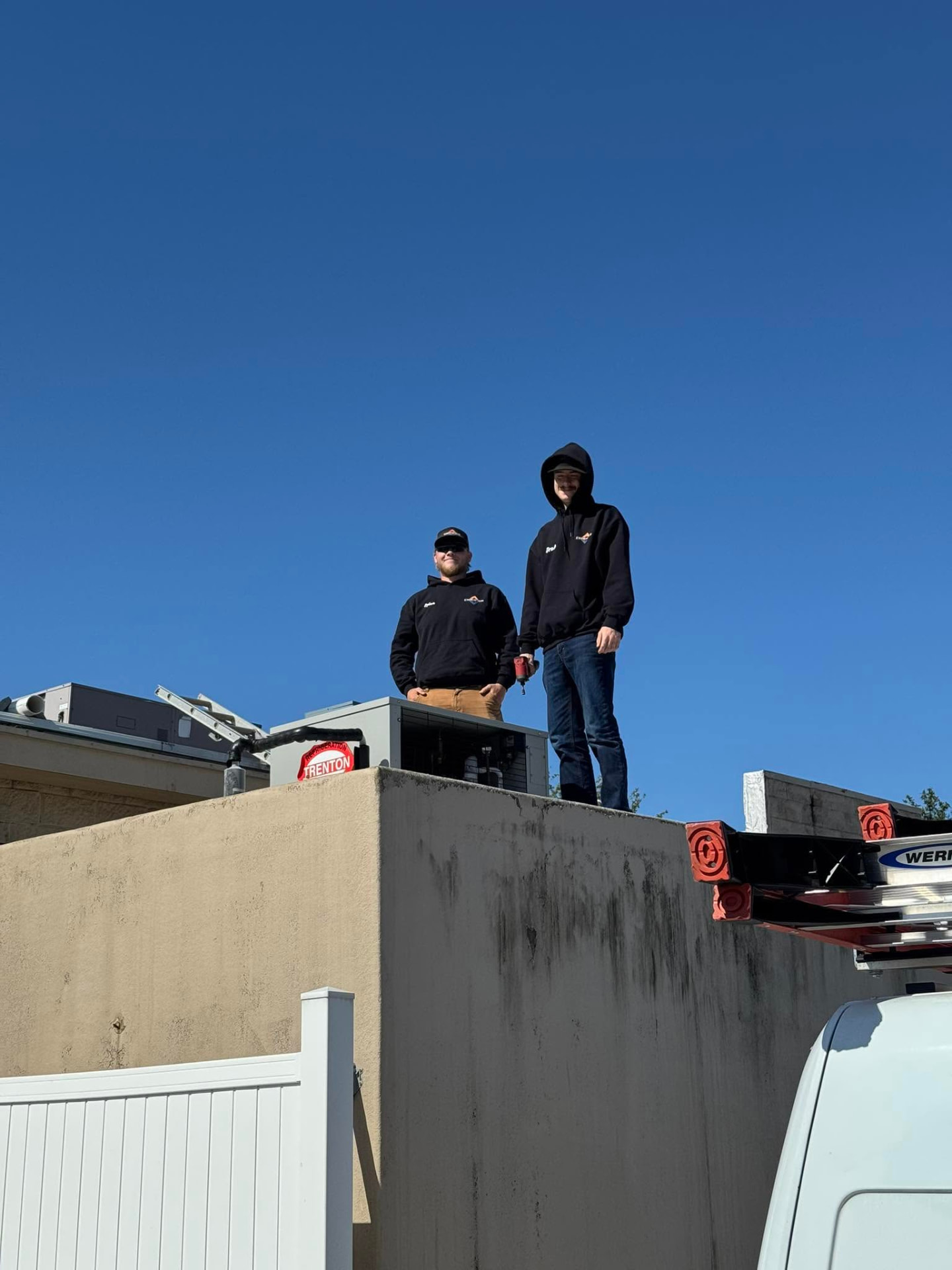Two 32 Heating and Cooling technicians on a rooftop beside commercial HVAC equipment